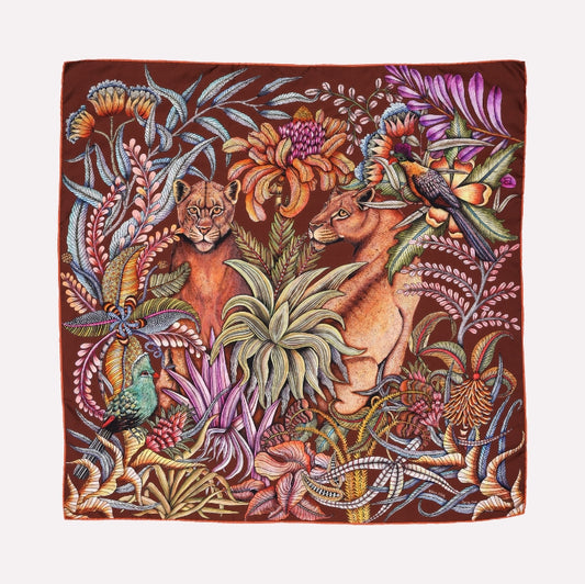 A square silk scarf featuring two silhouetted lionesses amid a lush, entangled African forest, with vibrant mahogany tones and intricate botanical details.