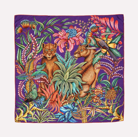 A vibrant silk scarf featuring two silhouetted lionesses among lush foliage, surrounded by exotic flowers and wildlife in a rich purple and multicolour palette.