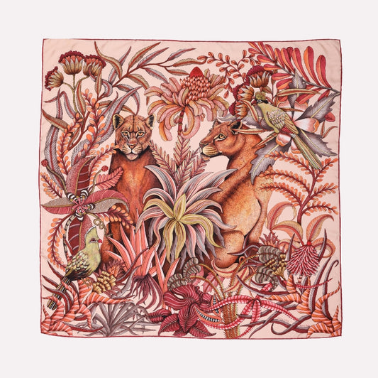 A silk scarf featuring two lionesses resting in a vibrant jungle scene, surrounded by rich red and flamingo-coloured botanical elements.