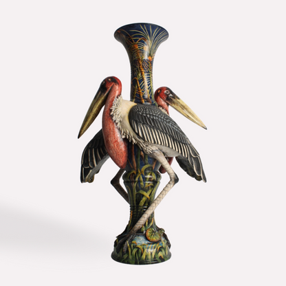 A tall, intricately sculpted ceramic vase featuring two Marabou Storks perched gracefully on either side. Their long legs and curved beaks are finely detailed, complementing the earthy tones and wetland-inspired base.