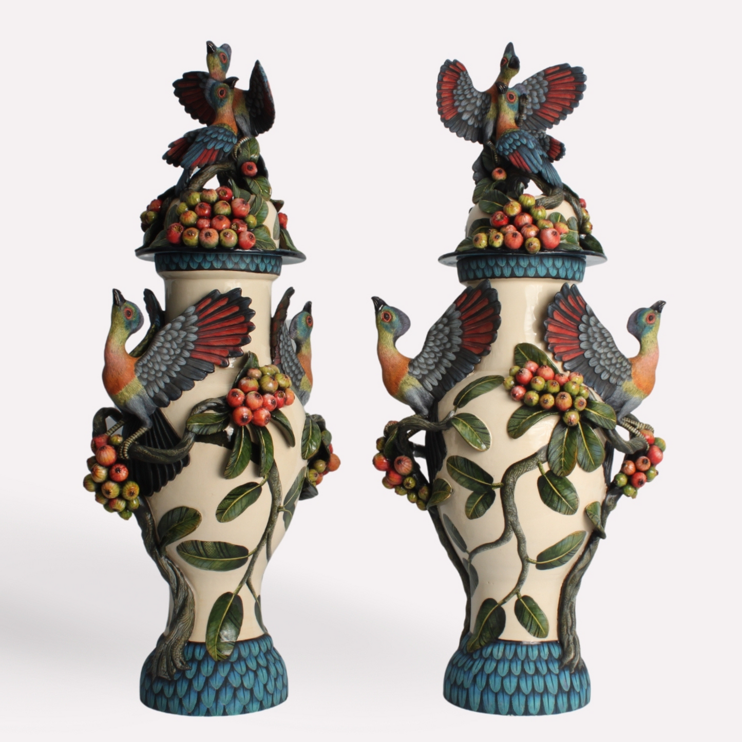 A pair of intricately designed urns featuring Purple Crested Turaco birds perched atop the lids. The urns are adorned with sculpted wild figs and detailed hand-painted patterns, symbolising freedom and abundance.