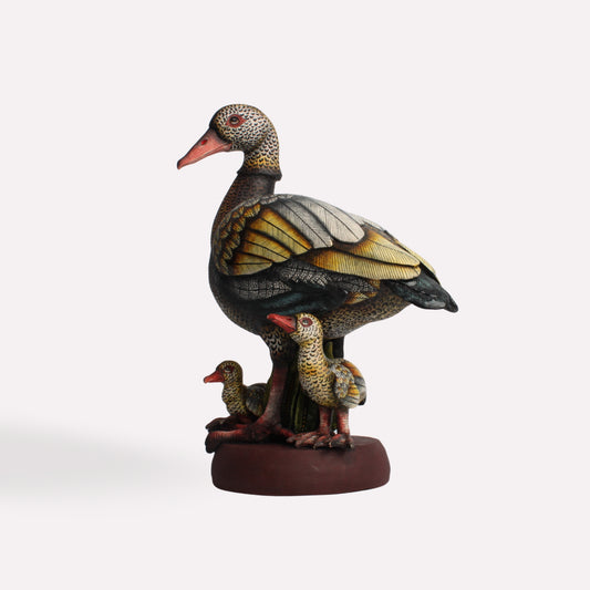 A finely sculpted ceramic artwork featuring an Egyptian goose standing protectively over its three goslings. The bird’s body is intricately painted with earthy tones and realistic feather detailing, creating a striking display of craftsmanship.