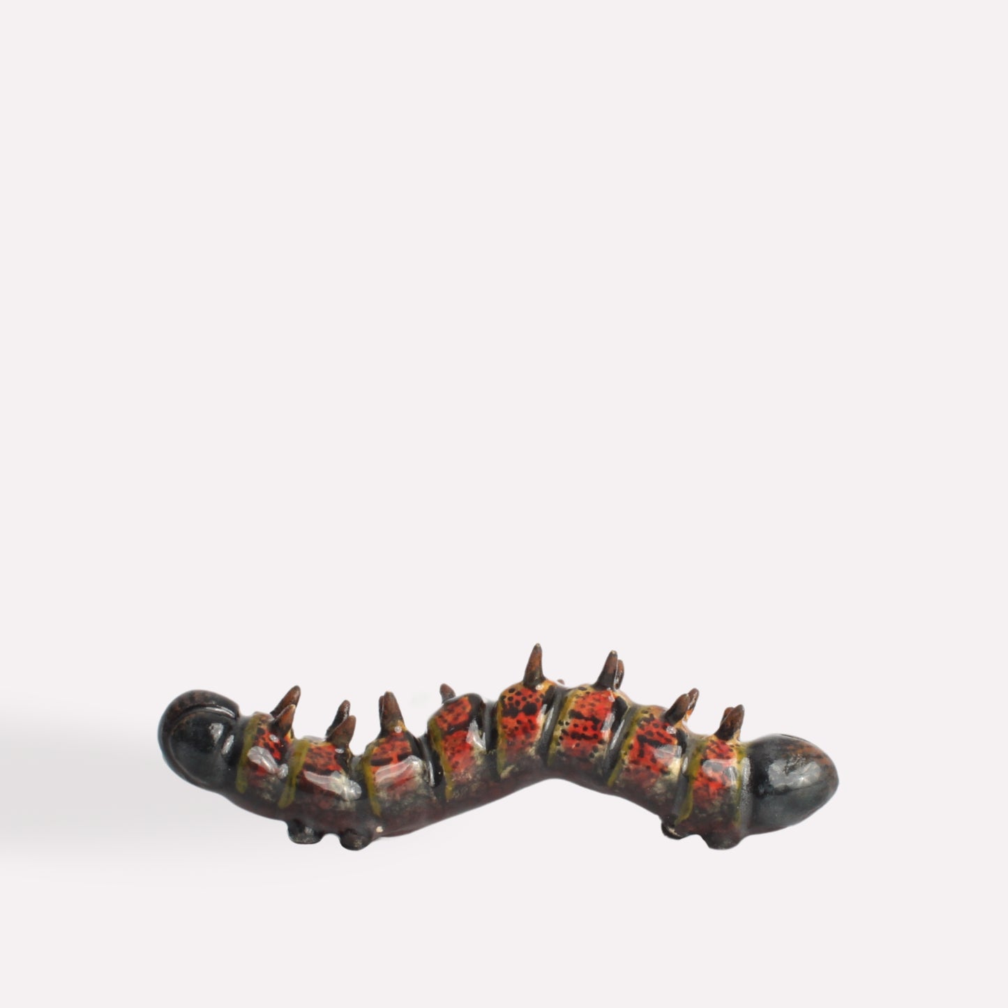 A side-angle view of the ceramic caterpillar, showing its textured body, vibrant colour pattern, and lifelike sculpting.