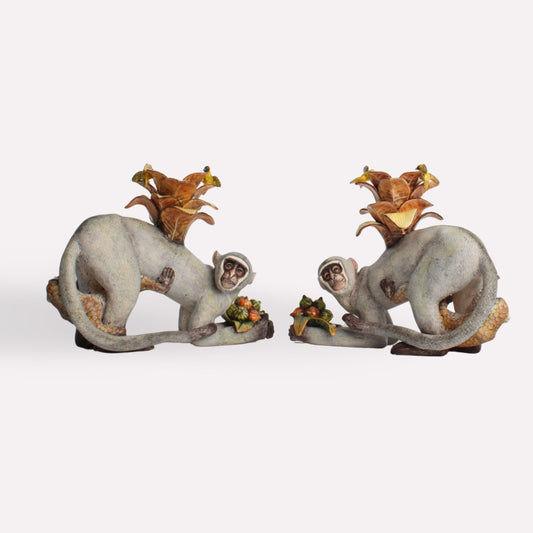 A pair of hand-sculpted ceramic monkey candle holders, each featuring a playful monkey with a golden-brown baby monkey on its back, holding space for a candle.