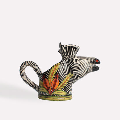 A ceramic jug intricately sculpted into the shape of a zebra's head, featuring bold black and white stripes, a curved handle, and vibrant hand-painted African flora.