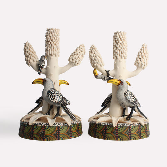 A pair of intricately designed candle holders featuring sculpted hornbills perched on a textured, tree-like structure. The base is detailed with artistic patterns, enhancing the natural theme.