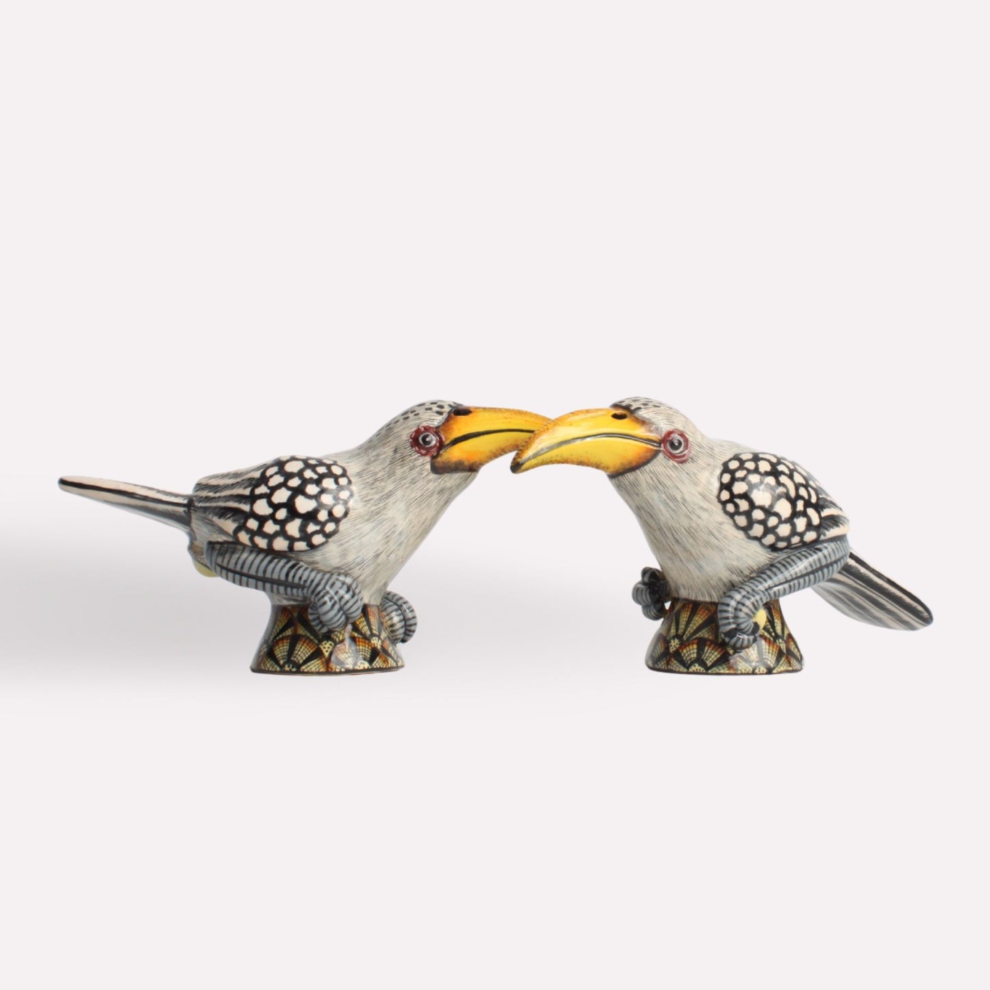 A pair of intricately designed ceramic hornbill-shaped salt and pepper shakers facing each other with their curved yellow beaks touching. Their detailed black-and-white feather patterns add a sophisticated and artistic touch.