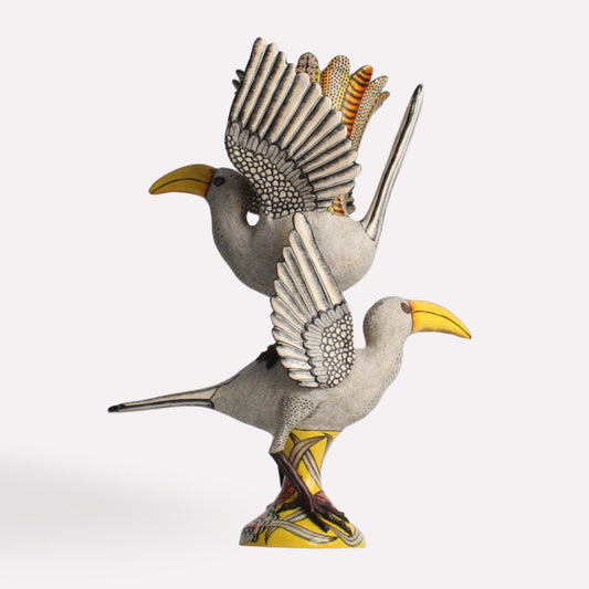 A striking ceramic vase sculpted in the shape of a hornbill with outstretched wings. The vase features intricate feather detailing, a curved yellow beak, and a base adorned with earthy patterns.