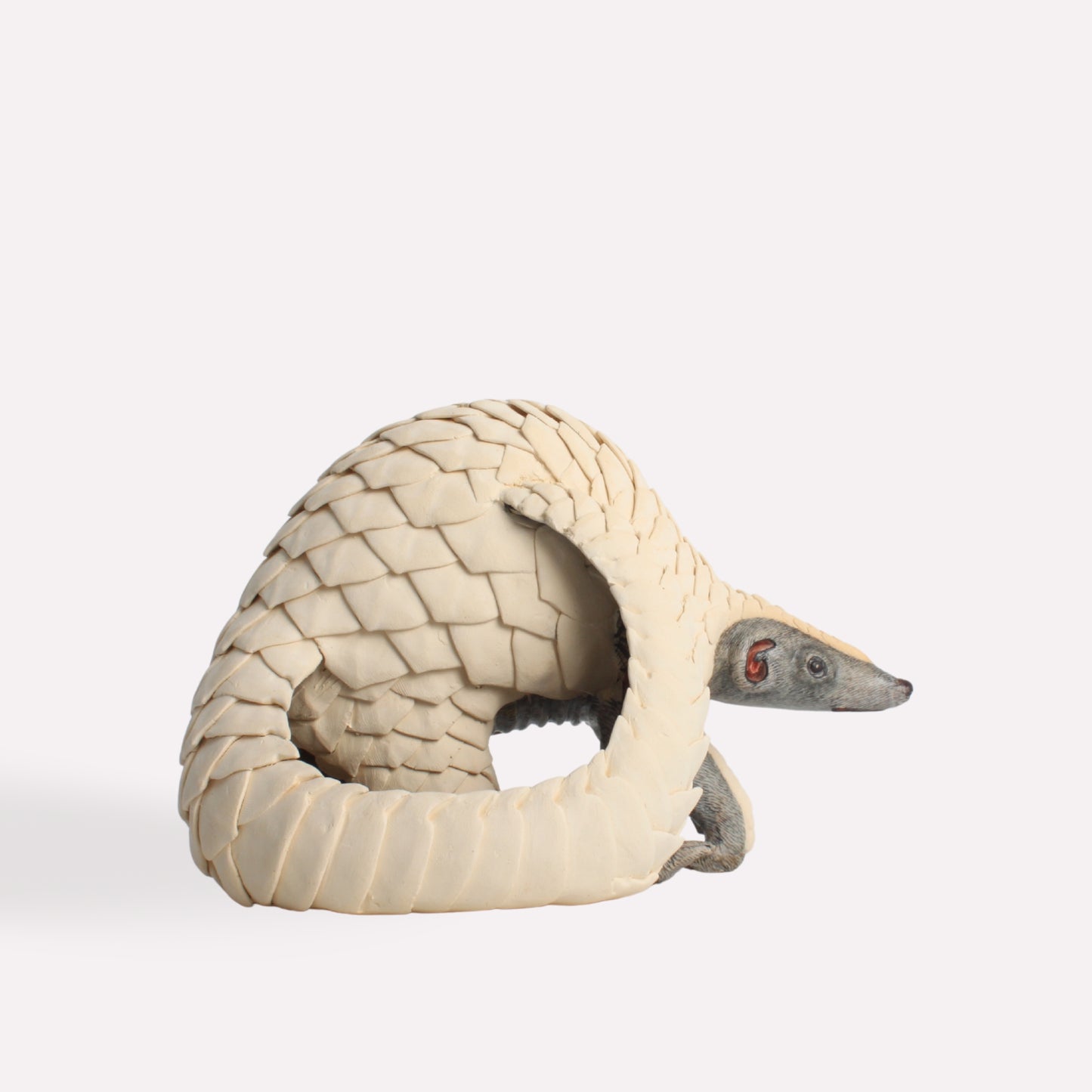 A profile shot of the pangolin sculpture, highlighting its elongated snout, delicate facial features, and intricate scale pattern wrapping around its body.