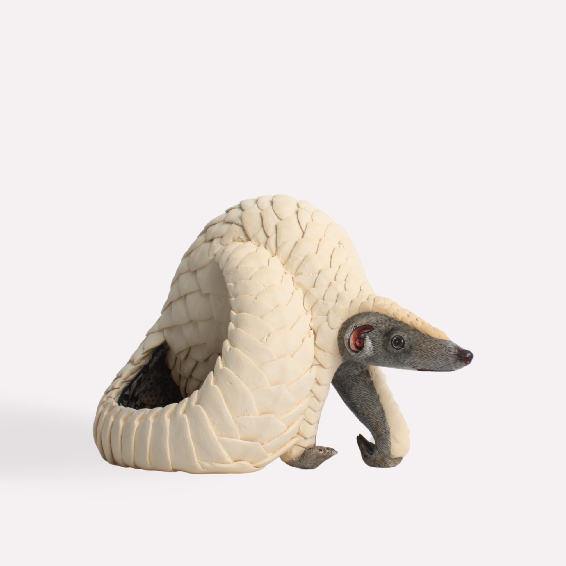 A detailed ceramic sculpture of a pangolin in a curled defensive posture, showcasing its meticulously crafted and textured scales in an ivory hue.