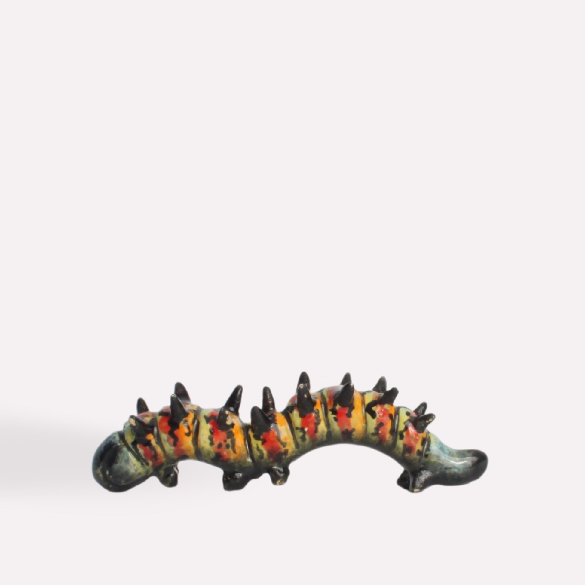 A side-angle view of the ceramic caterpillar, showing its textured body, vibrant colour pattern, and lifelike sculpting.