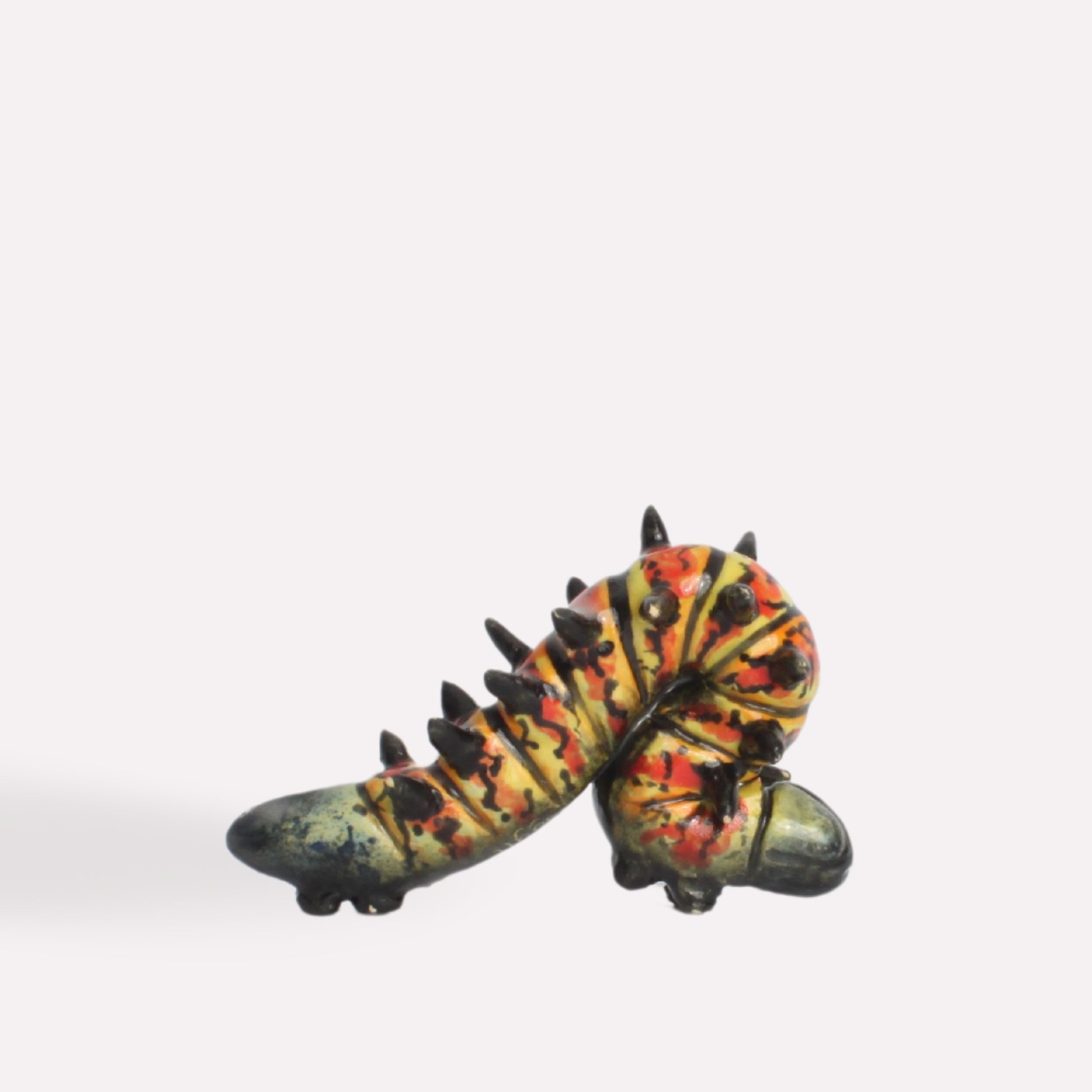 A side-angle view of the ceramic caterpillar, showing its textured body, vibrant colour pattern, and lifelike sculpting.