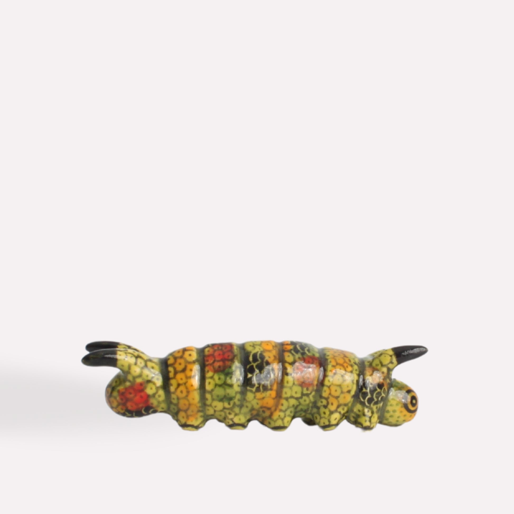 A hand-painted ceramic caterpillar sculpture with a segmented body in vibrant yellow, green, and red tones, featuring small black antennae and legs.