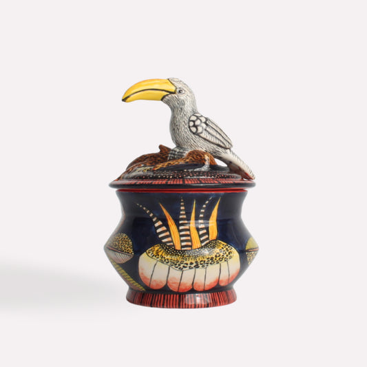 A handcrafted ceramic trinket box featuring a black base with intricate hand-painted botanical patterns, topped with a sculpted yellow-billed hornbill figurine.