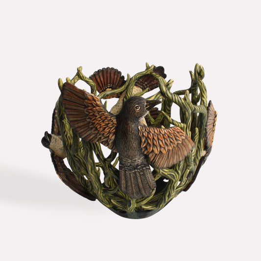 A handcrafted ceramic vessel featuring an intricate design of coucal birds perched within a sculpted network of branches. The birds’ feathers are painted in warm earthy tones, contrasting with the deep green foliage.