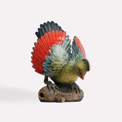 A hand-sculpted ceramic Turaco bird with vibrant green plumage, a red crest, and detailed feather patterns. The bird is perched on a textured base.