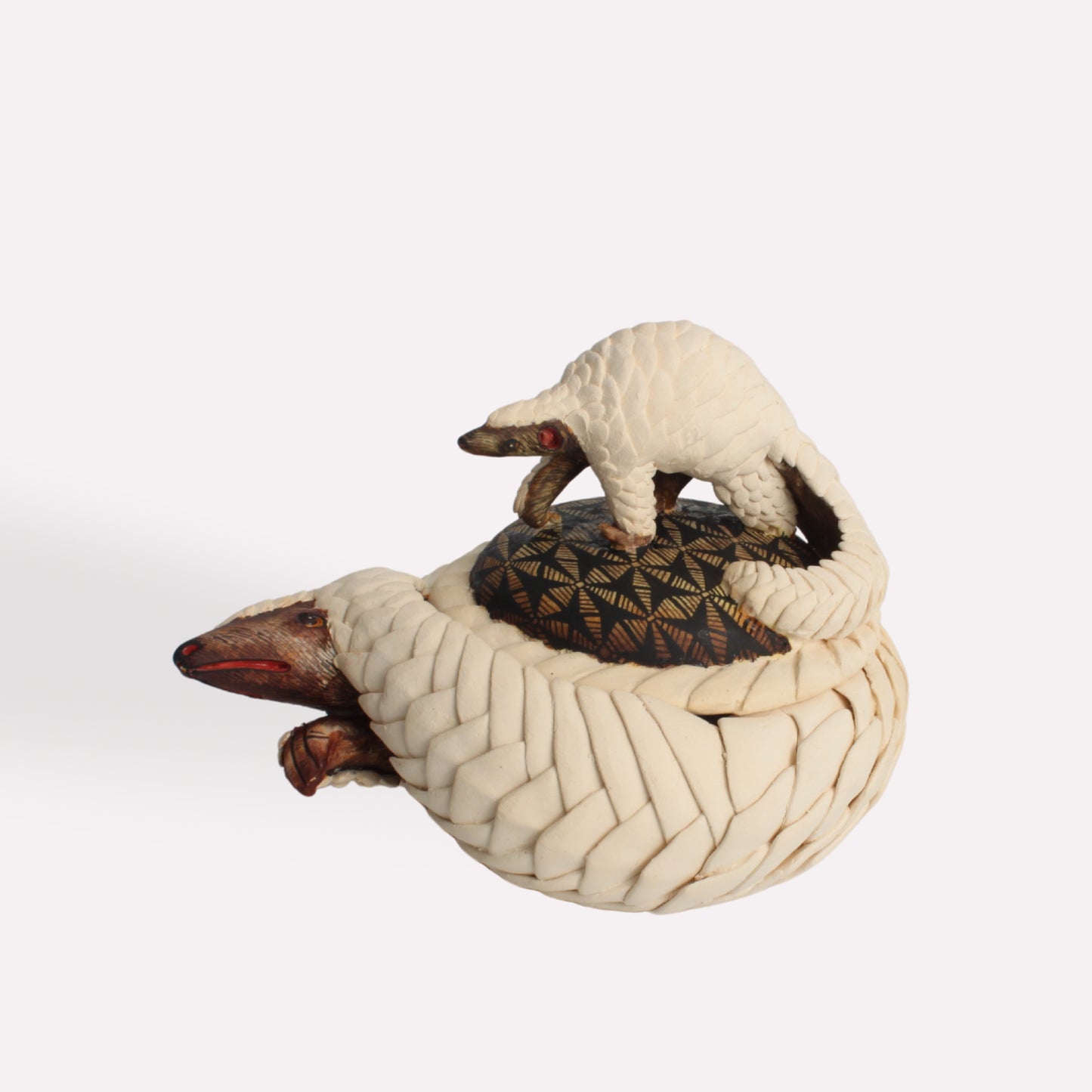 A handcrafted ceramic trinket box in the shape of a curled pangolin. The lid features a detailed pangolin figure resting atop a textured surface, with intricate hand-painted scales and earthy tones.