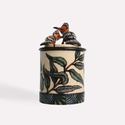 A three-quarter view of the ceramic candle container, highlighting its sculpted bird lid and botanical motifs.