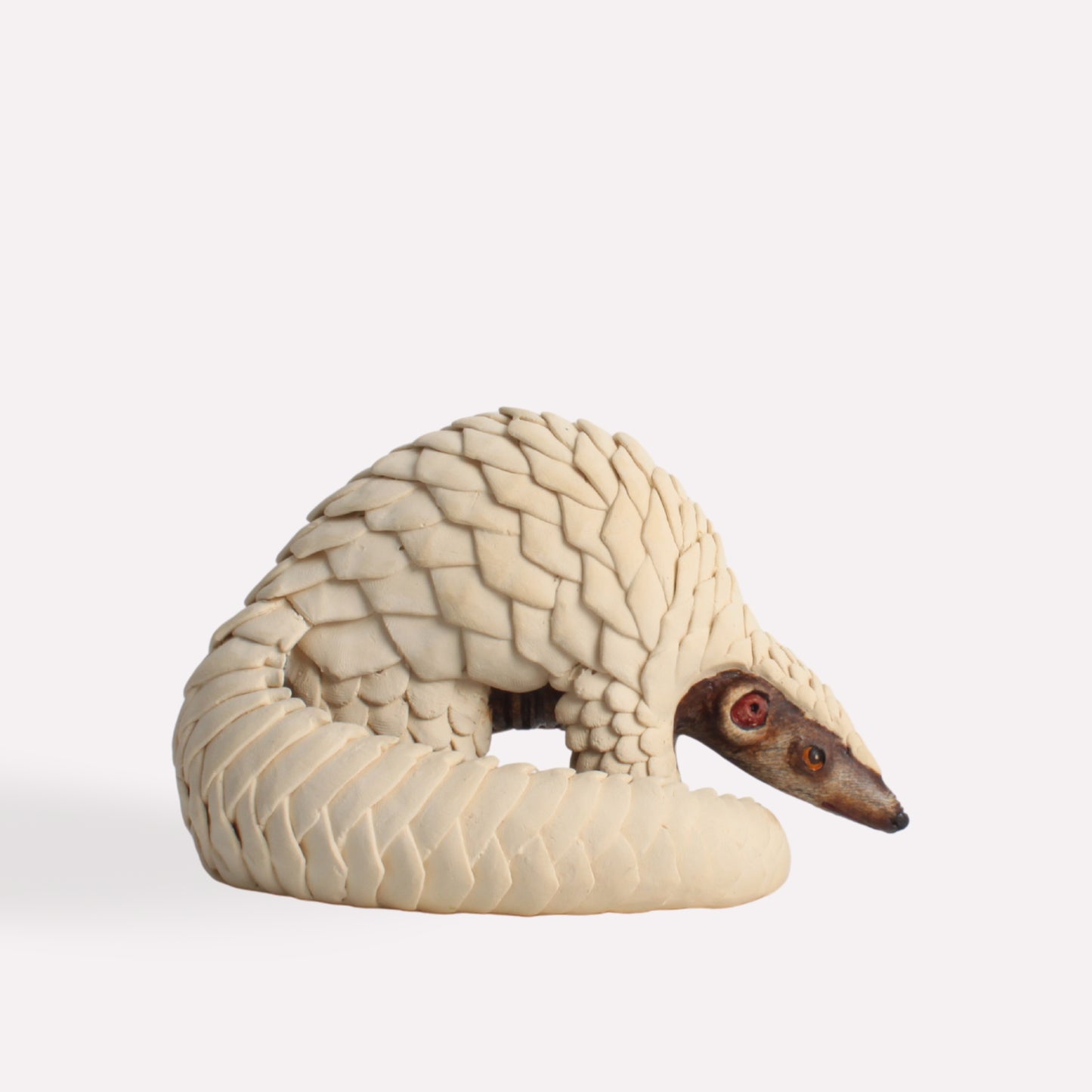 A handcrafted ceramic sculpture of a pangolin, showcasing its curved body and intricately textured scales in an ivory hue, with lifelike facial details.