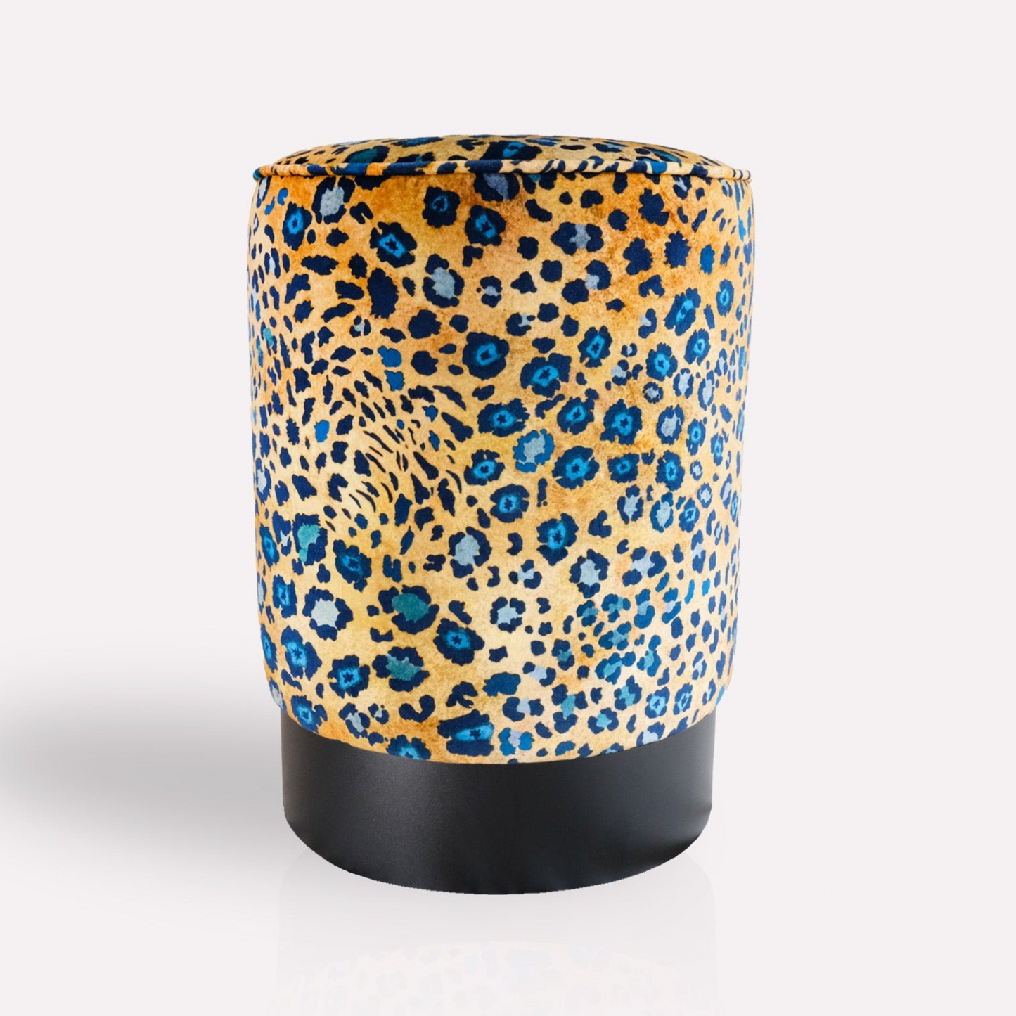 A cylindrical velvet pouffe with a striking blue and gold leopard-spot-inspired pattern, resting on a sleek black brass base.