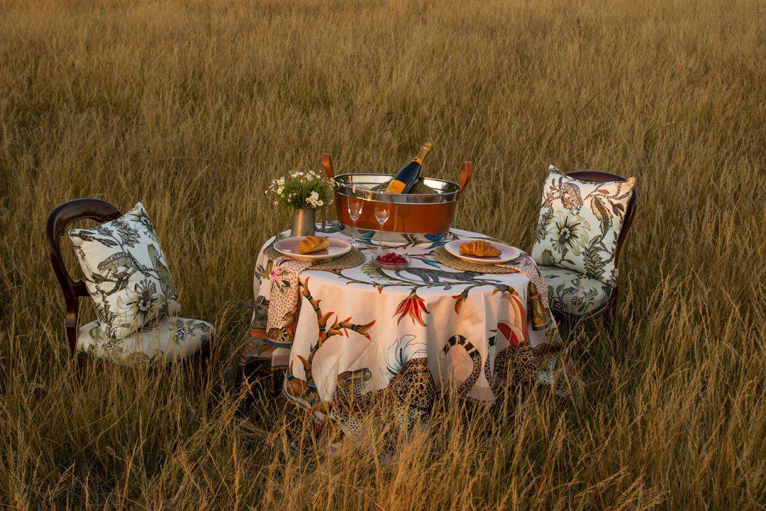 A broader perspective showcasing the tablecloth in an open field, blending seamlessly with its surroundings to create a luxurious safari-themed aesthetic.