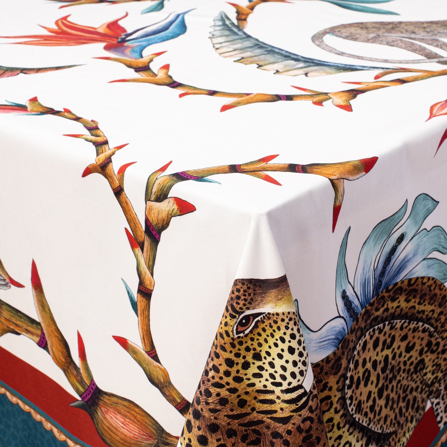 A close-up of the Monkey Paradise Square Tablecloth draped over a table, showcasing its vibrant animal and botanical patterns.